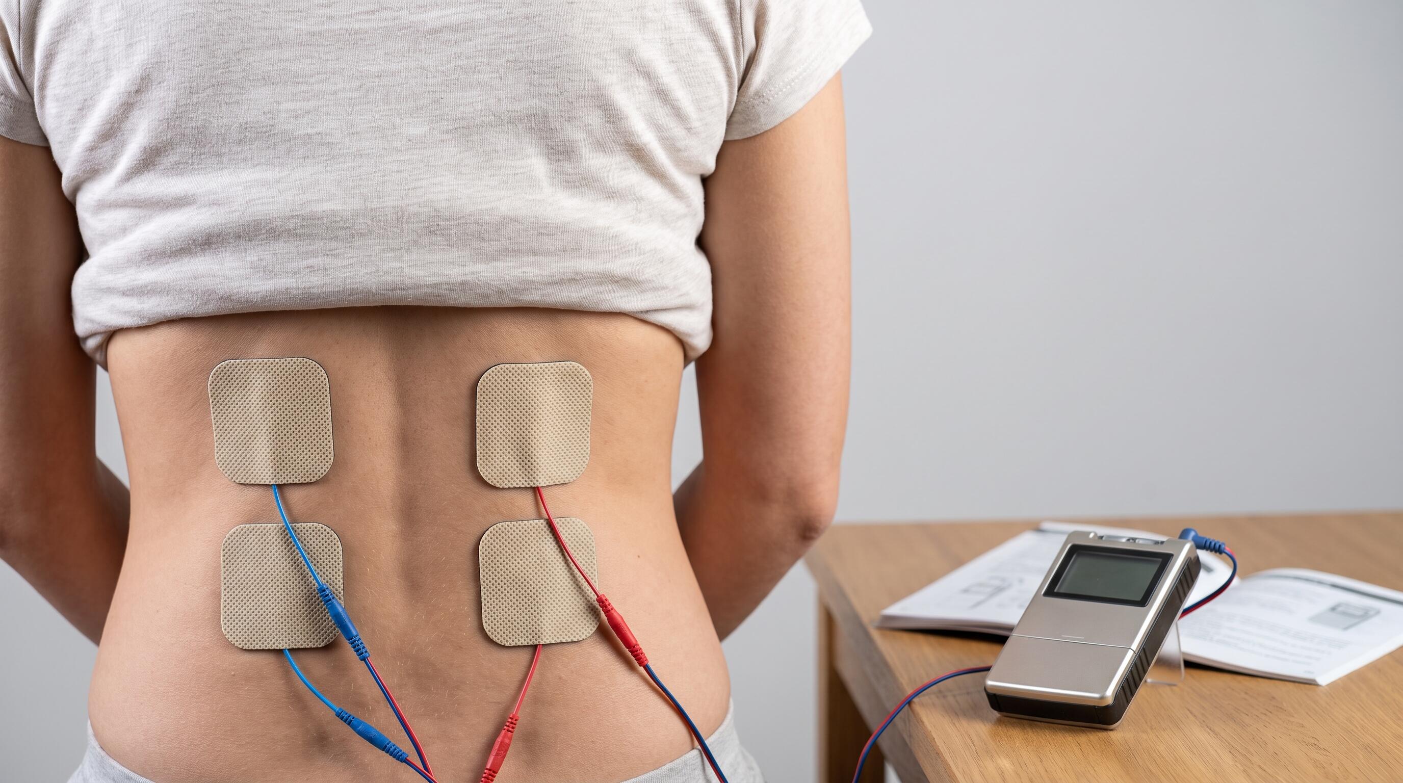 Person placing electrode pads on lower back for TENS EMS physical therapy support at home